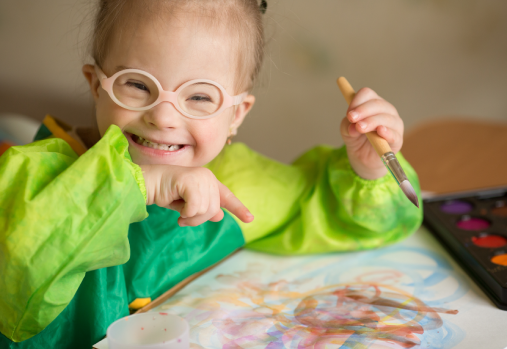 Un petit enfant portant des lunettes et une blouse de peintre créant des œuvres d'art avec un pinceau.