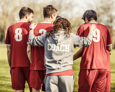 Coach with arm around soccer players in a team huddle.