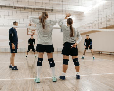 Indoor volleyball game with players preparing for a serve at the net.