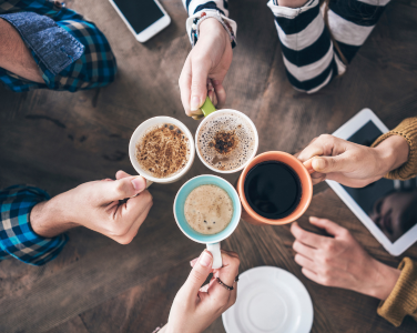 Des mains tenant des tasses à café colorées au-dessus d'une table en bois.