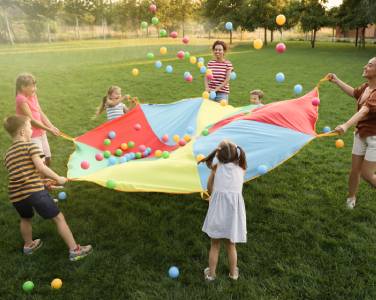 enfants qui jouent dehors avec un parachute et des balles