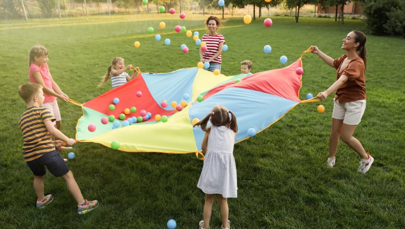 enfants qui jouent dehors avec un parachute et des balles