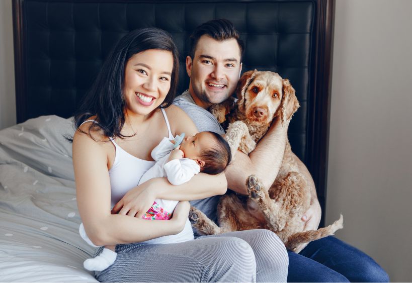 jeune famille avec bébé et chien assis sur un lit
