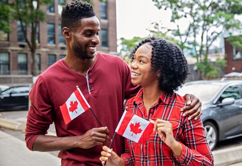 Un couple souriant tenant des drapeaux canadiens.