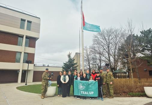 Groupe de civils et de membres des FAC devant le drapeau Teal Up hissé