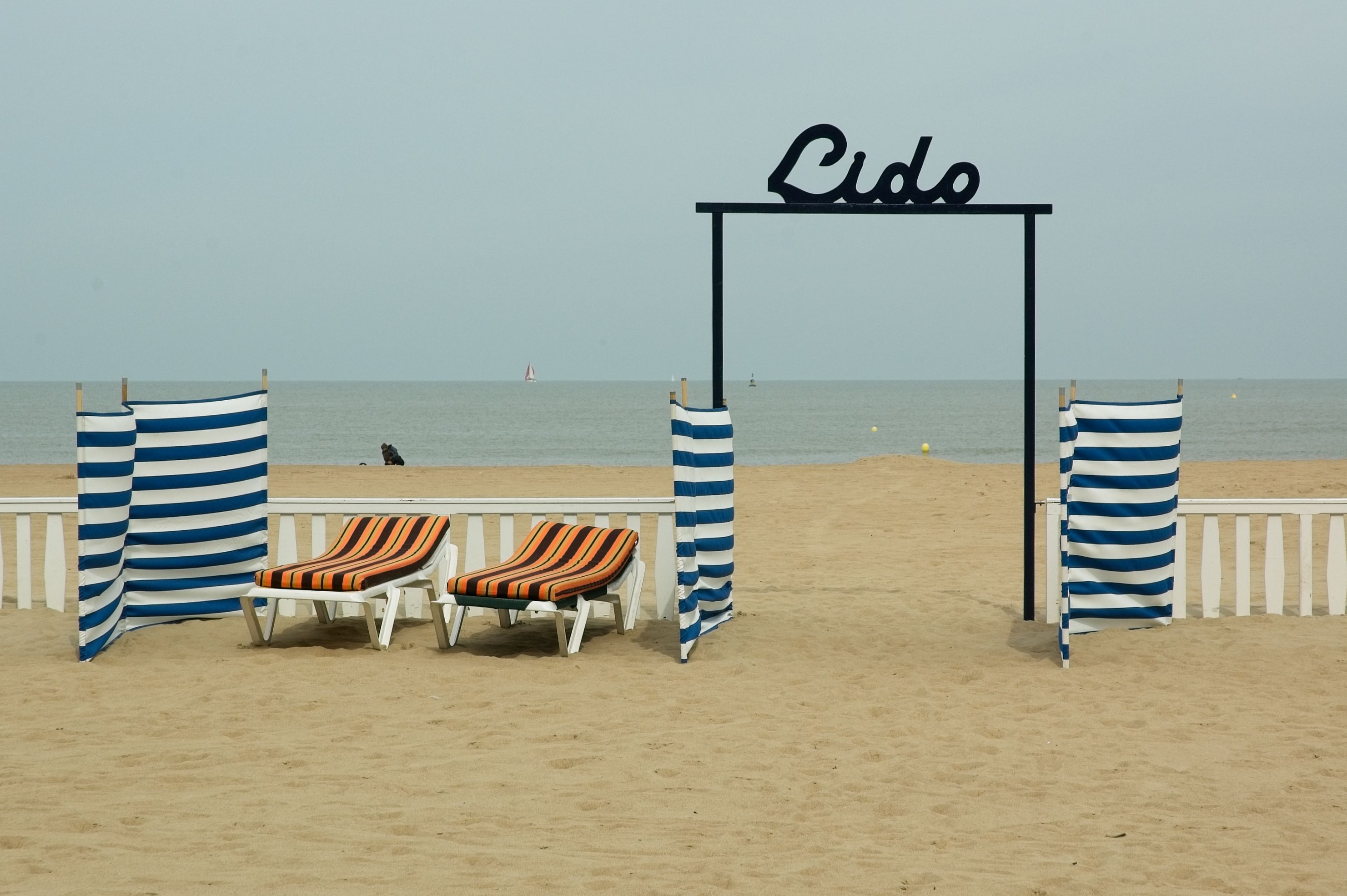 Scène de plage apaisante avec des transats, des auvents rayés et une vue sur la mer sous l'entrée du Lido.