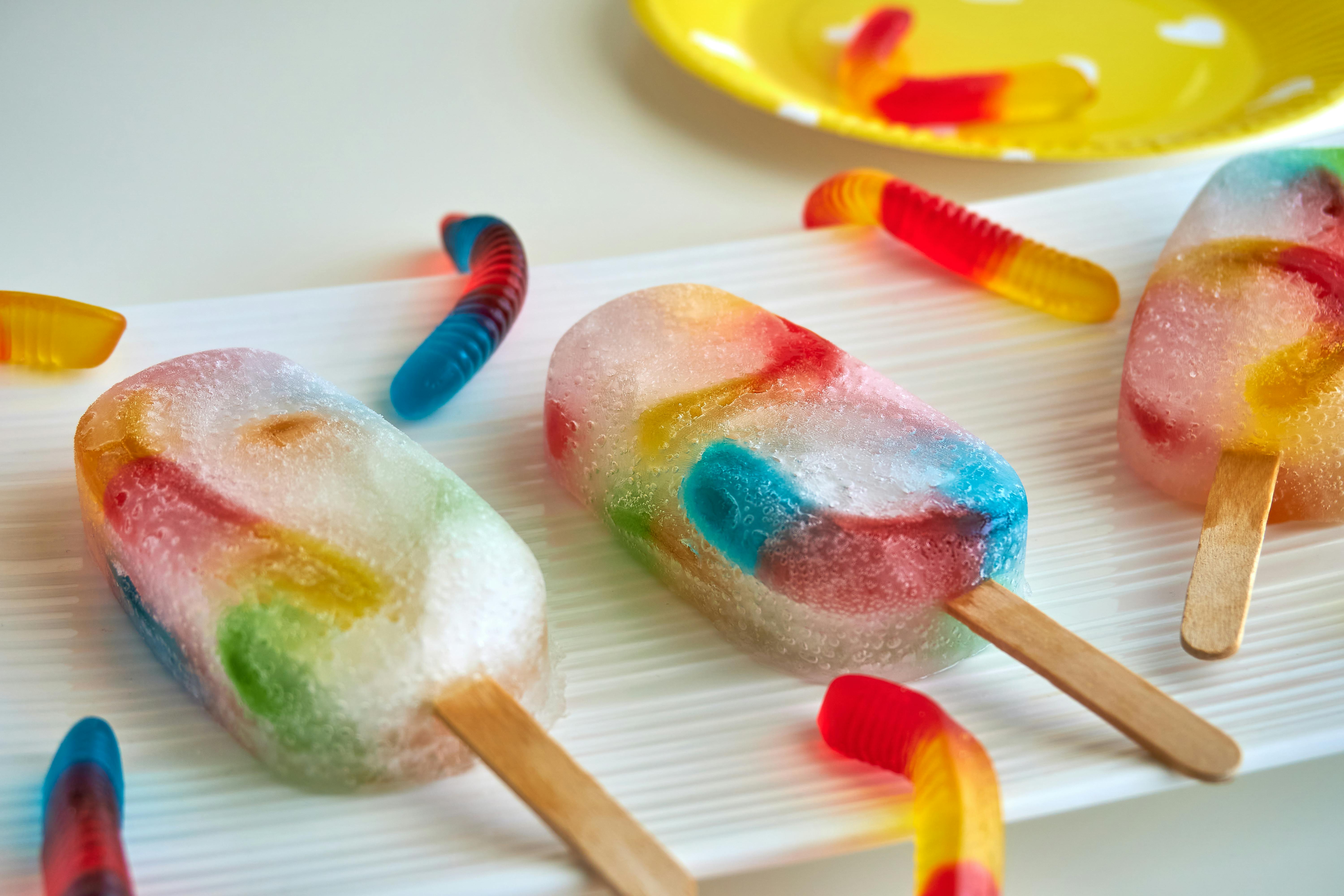 des glaces à l'eau avec des vers en gélatine posées sur un plan de travail