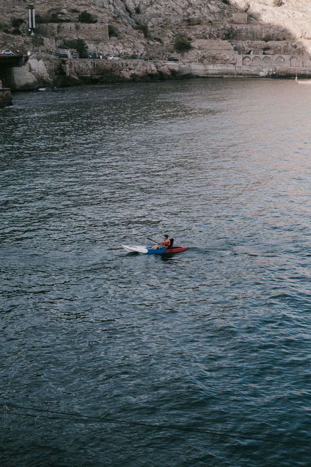 Un kayakiste pagaye dans les eaux côtières paisibles, entouré de falaises rocheuses, dans un plan vertical dynamique.
