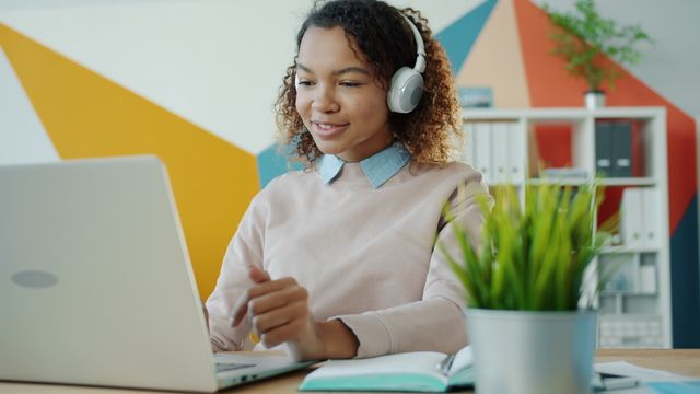 Jeune femme utilisant un ordinateur portable et portant un casque d’écoute dans un environnement de bureau moderne.