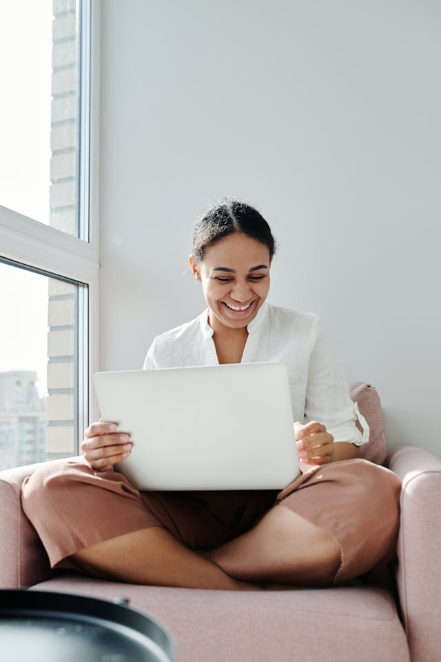 une personne assise sur une chaise, souriant à son ordinateur portable