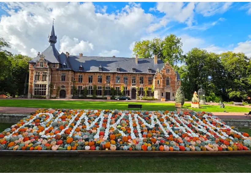 Un manoir historique se dresse derrière une grande exposition décorative de citrouilles colorées aménagée dans un jardin à la française.