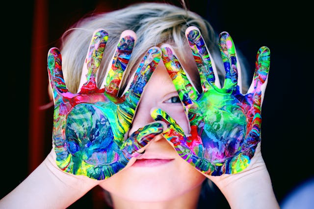 Gros plan vibrant des mains d’un enfant couvertes de peinture colorée, exprimant créativité et plaisir.