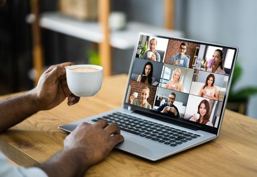 Personne tenant une tasse de café tout en regardant une rencontre en ligne sur un ordinateur portable