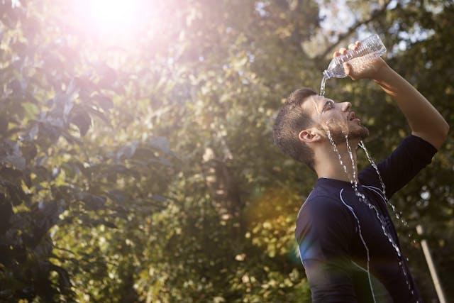 Un homme en t-shirt bleu à col rond en train de se verser de l'eau sur le visage