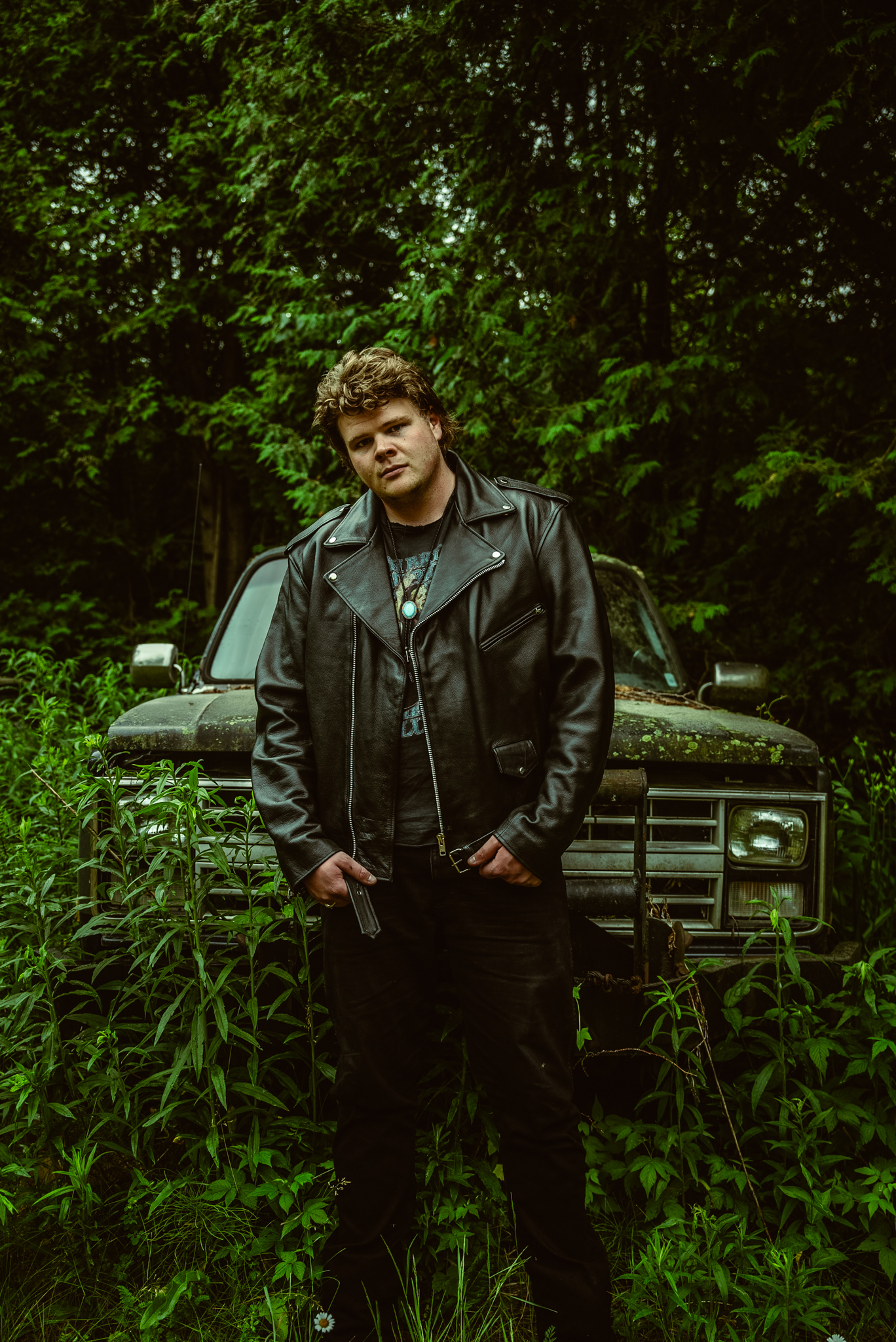 Brayden King standing in front of a vintage truck among green foliage