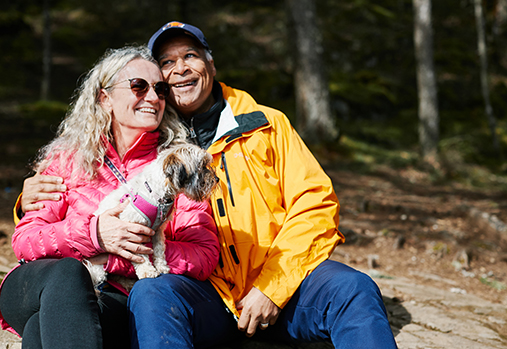 man and woman sitting in the wood with a dog