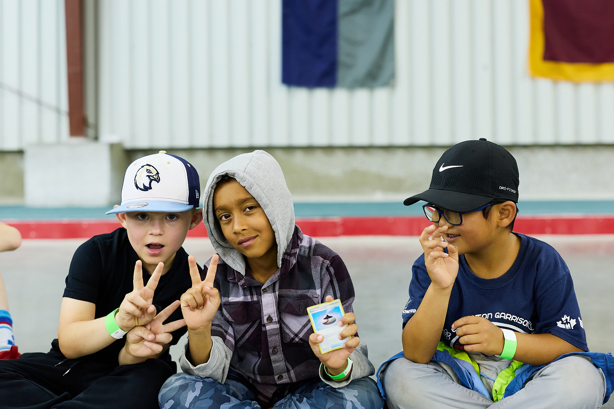 Trois enfants d’âge scolaire souriants regardant la caméra et tenant une carte Pokémon. 