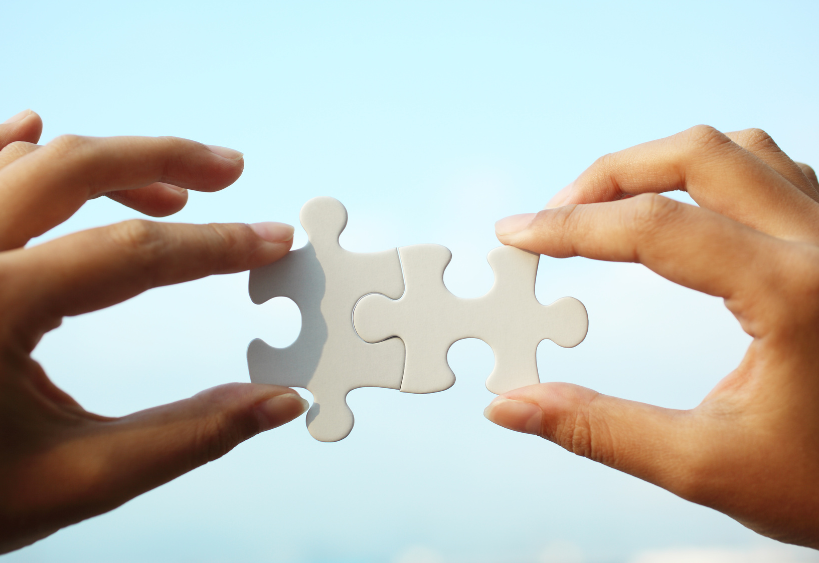 Deux mains prêtes à assembler les pièces d'un puzzle sous un ciel bleu limpide, capturant l'instant où la collaboration rencontre la clarté.