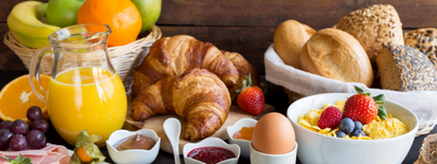 Un assortiment de déjeuner comprenant du jus d’orange, des croissants, des petits pains, des fruits, un bol de yogourt avec des baies, de la confiture et un œuf à la coque sur une table en bois.